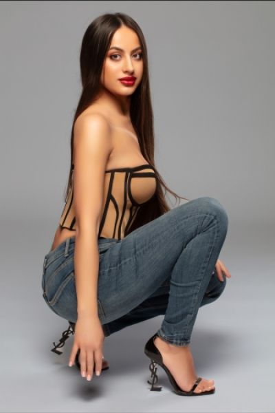 A sexy brunette lady with red lips pictured wearing jeans and strappy high heels 